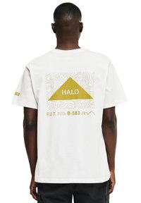 Osoba ubrana w białą koszulkę z żółtym trójkątem i motywem mapy topograficznej, oznaczona napisem "HALO" oraz tekstem "F.U.T. Wychowanie fizyczne i trening" na plecach.