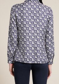 Navy and white patterned blouse featuring a geometric design, long sleeves, buttoned cuffs, and a collared neckline. Smooth fabric texture.