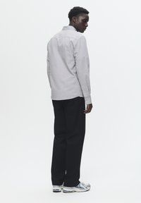 Camisa abotonada gris con un acabado texturizado, pantalones negros y zapatillas deportivas plateadas. Muestra un diseño simple y clásico desde una perspectiva lateral.