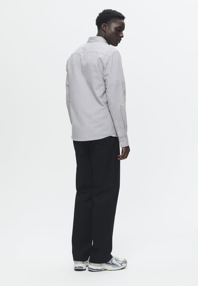 Chemise grise à manches longues avec une finition texturée, pantalon noir et chaussures de sport argentées. Présente un design simple et classique vu de profil.