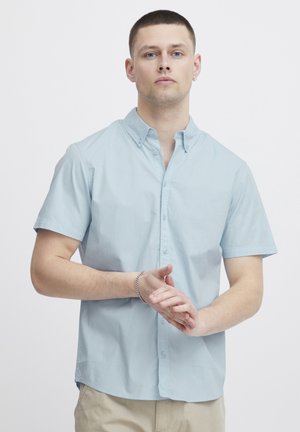 Chemise à manches courtes bleu clair, en coton, avec un col classique et une texture subtile. Elle présente un devant à boutons et une coupe décontractée.