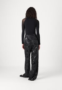 Top nero a maniche lunghe con maniche trasparenti abbinato a pantaloni neri a gamba larga con paillettes, caratterizzati da un motivo testurizzato e una superficie lucida.