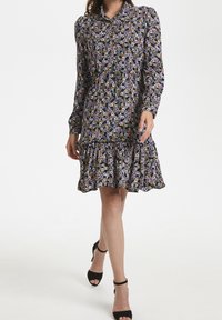 Abito a camicia floreale con maniche lunghe, sfondo nero, fiori viola e arancioni, orlo arricciato e vestibilità comoda.