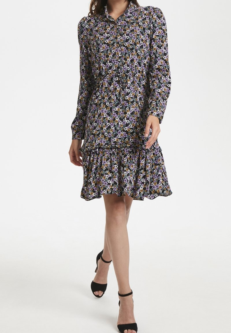 Abito a camicia floreale con maniche lunghe, sfondo nero, fiori viola e arancioni, orlo arricciato e vestibilità comoda.