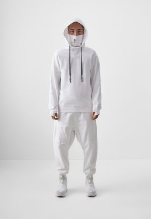 White hooded sweatshirt with drawstrings and matching baggy pants. Features face mask, textured fabric, and visible patch pockets.
