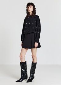 Felpa nera con decorazioni in perle testurizzate, abbinata a una gonna nera a campana e stivali neri lucidi al ginocchio con punta affusolata.