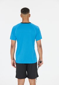 Blå idrottströja med svart krage, korta ärmar och en mjuk yta; kombinerad med svarta shorts och håller en racket.