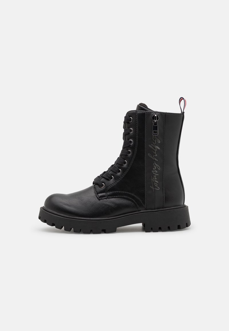Botte de combat en cuir noir avec semelle épaisse à crampons, lacets à l'avant, fermeture éclair latérale et bande de marque à la cheville.