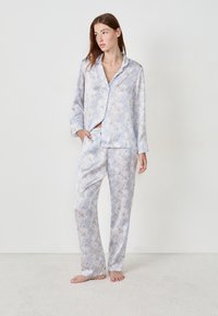 Lichtblauwe pyjamastel met bloemenpatroon, gemaakt van een gladde stof. Bevat een button-up shirt en bijpassende broeken met een elastische tailleband.