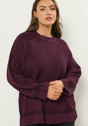 Pull en maille violet surdimensionné avec texture côtelée, détails brodés noirs sur les manches et encolure ronde.