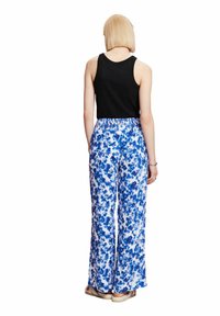 Svart linne i kombination med vida byxor med ett blått blommönster på vit bakgrund; elastisk midja, avslappnad passform.