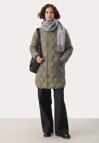 Vadderad olivgrön jacka med diamantkviltat mönster, frontdragkedja och sidofickor, tillsammans med en grå scarf och svarta byxor.