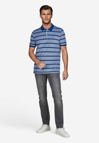 Gestreepte polo voor heren in blauwtinten met een donkerblauwe kraag, gecombineerd met grijze jeans en witte sneakers. Glad materiaal, korte mouwen.