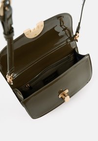 Crossbody-Tasche aus olivgrünem Lackleder mit einem goldfarbenen Verschluss, ausgestattet mit einer Reißverschlusstasche und zwei Innenfächern.