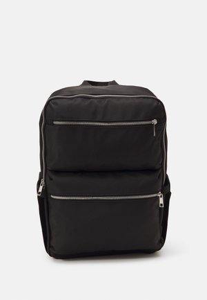 Mochila negra con un diseño elegante, que cuenta con dos bolsillos frontales con cremallera, cuerpo acolchado y detalles en hardware plateado. Textura suave.