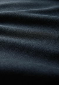 Zachte, donker marineblauwe stof met subtiele diagonale weving en zachte plooien die een gladde, vloeiende textuur en lichtreflecties creëren.