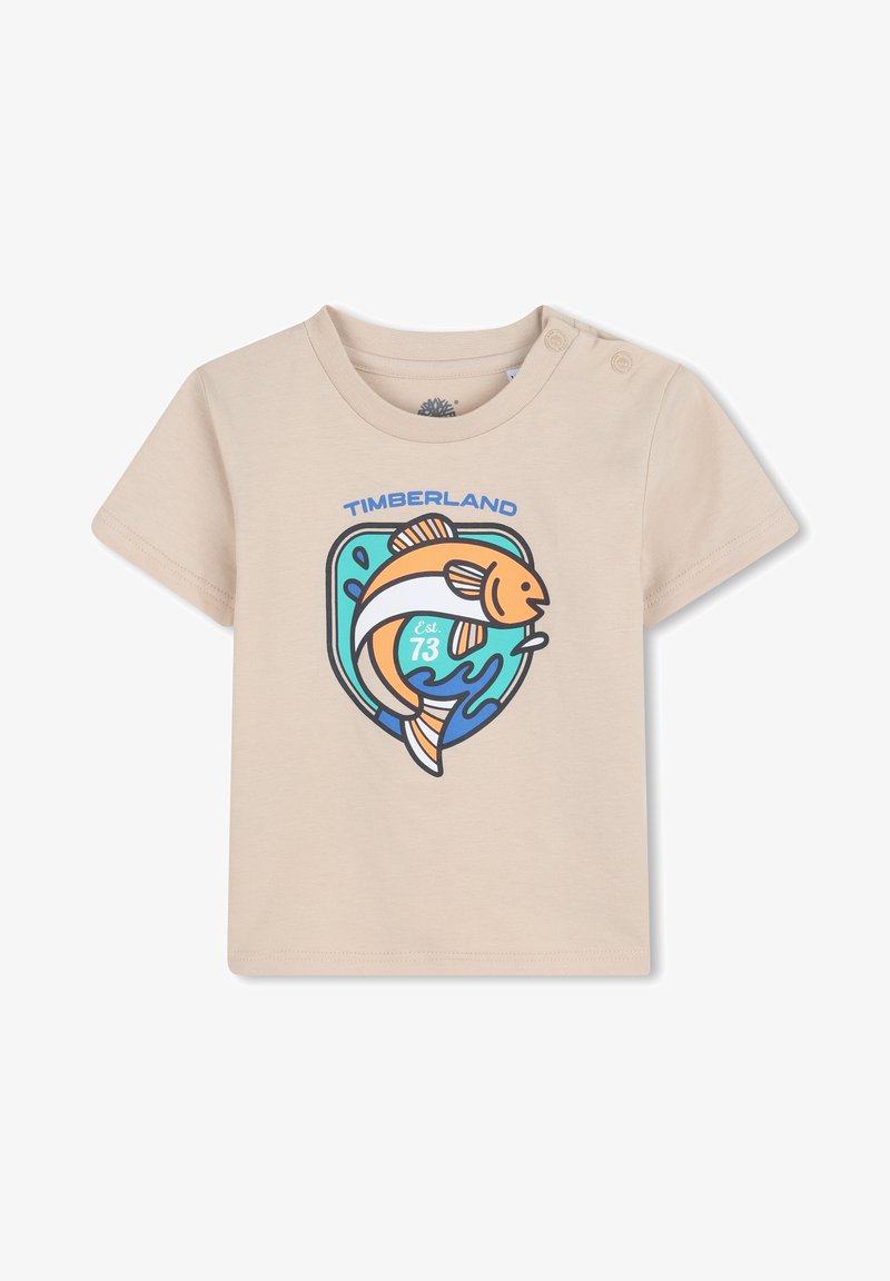 T-shirt en coton beige à manches courtes, avec un graphisme coloré de poisson et le texte "TIMBERLAND" en bleu et orange. Détail bouton pression sur l'épaule.