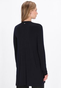 Marineblauer Langarmpullover mit rundem Ausschnitt, weicher Textur und einem kleinen Logoverweis auf der Rückseite. Lässiger Schnitt mit einem leicht längeren Rückenteil.