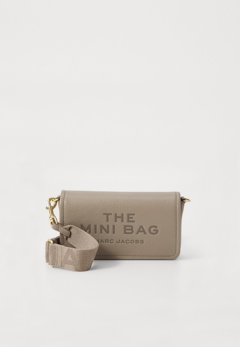 Bežna mini torbica iz umetne usnja z zlatim dodatki, ki vsebuje vzorčeno besedilo "THE MINI BAG" in odstranljiv platneni trak.