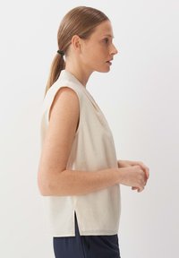 Top beige senza maniche con vestibilità rilassata, caratterizzato da un collo rotondo e leggere fessure laterali all'orlo. Tessuto morbido.