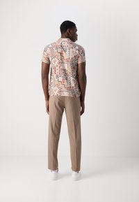 Kortærmet skjorte med et geometrisk print i beige, brune og røde nuancer; parret med beige bukser og hvide sneakers.