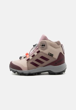 Botte de randonnée marron clair et rose avec des accents bordeaux, étiquette Gore-Tex et semelle noire robuste, vue de côté sur fond blanc.