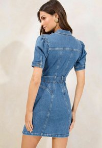 Denim suknelė su prigludusiu dizainu, trumpomis pūstomis rankovėmis ir diržo juostele. Šviesiai mėlyna spalva su matomomis siūlėmis ir pritaikyta siluetu.