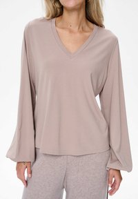 Langarm, V-hals top in zacht taupe stof met een relaxte pasvorm en iets uitlopende mouwen, gecombineerd met bijpassende lichtgrijze broek.
