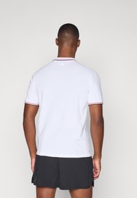 Hvit polo med flat krage og røde og marineblå striper på kantene. Korte ermer og avslappet passform. Bært med svarte shorts.