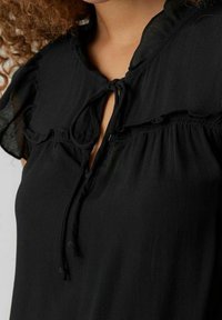 Blusa nera con scollo rotondo e chiusura con fiocco, maniche volant, tessuto morbido e vestibilità rilassata. Texture liscia con un leggero luccichio.