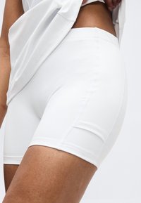 Κοντινό πλάνο ενός ατόμου που σηκώνει λευκό πουκάμισο για να αποκαλύψει στενά λευκά ποδηλατικά σορτς στο πάνω μέρος του μηρού και τη μέση.