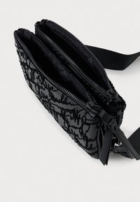 Borsa nera con zip e superficie texture, caratterizzata da un design di scrittura astratto. Tre scomparti con doppie zip e tracolla regolabile.