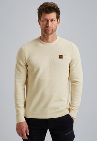 Crème-kleurige sweatshirt met een ronde hals, voorzien van een geweven patroon en een klein bruin logo-opdruk op de borst.