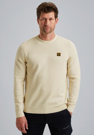 Crème-kleurige sweatshirt met een ronde hals, voorzien van een geweven patroon en een klein bruin logo-opdruk op de borst.