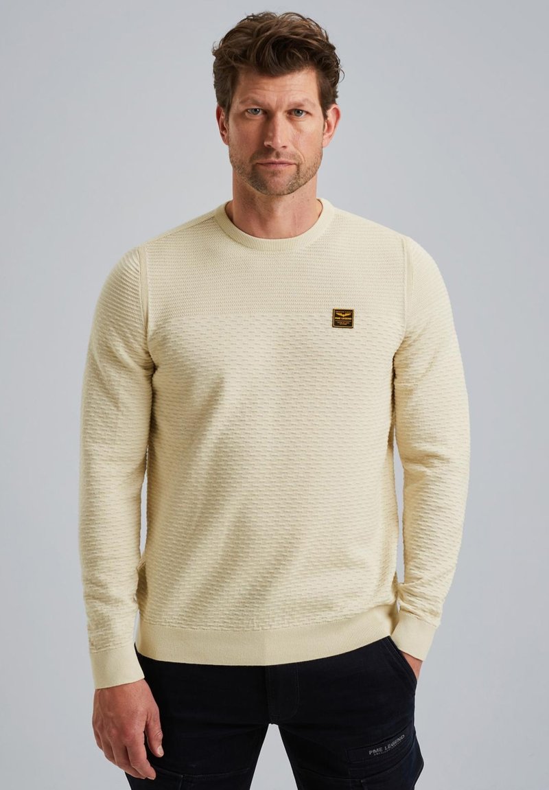 Crème-kleurige sweatshirt met een ronde hals, voorzien van een geweven patroon en een klein bruin logo-opdruk op de borst.