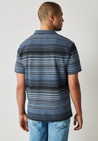 Pruhovaná polo košile s různými modrými a černými vodorovnými pruhy, krátkými rukávy a plochým límečkem. Měkká, strukturovaná tkanina.