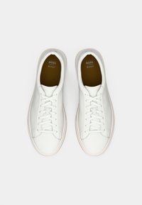 Weiße Leder-Sneaker mit glatter Textur, die ein niedriges Profil, ein schnürbares Design und Gummisohlen aufweisen. Innen zeigt sich eine braune Einlegesohle mit Branding.