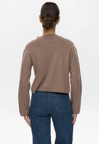 Maglione marrone tagliato con maniche lunghe, scollatura a coste e tessuto testurizzato. Abbinato a jeans blu a righe sottili con vita alta.