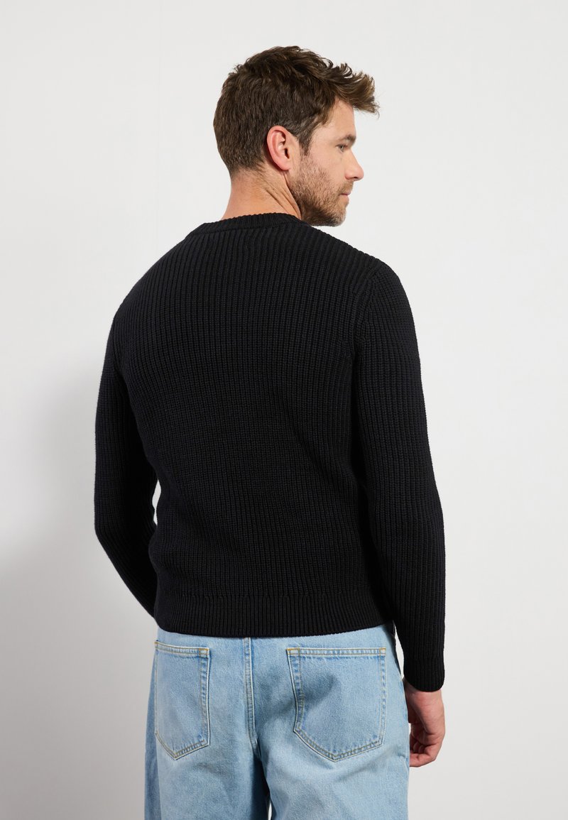 Maglione nero a coste con maniche lunghe e collo rotondo, mostrato da dietro. Tessuto morbido, design aderente, abbinato a jeans blu chiaro.