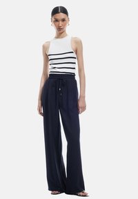 Witte tanktop met zwarte strepen, gecombineerd met losse, donkerblauwe broek met een elastische tailleband en trekkoorddetail.