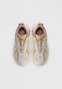 Sportlich aussehende Schuhe mit einem atmungsaktiven grauen Mesh-Obermaterial, beigen Akzenten und einer strukturierten Sohle. Zu den Merkmalen gehören Schnürsenkel und eine Schlaufe an der Ferse.