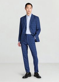 Marineblauer Anzug mit Karomuster, bestehend aus einem Blazer mit einem Knopf, maßgeschneiderten Hosen und einem hellblauen Hemd. Schwarze Elegante Schuhe.