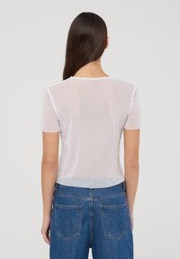 Top bianco in mesh a maniche corte con un motivo scintillante, texture trasparente e scollatura rotonda. Abbinato a jeans blu a vita alta.