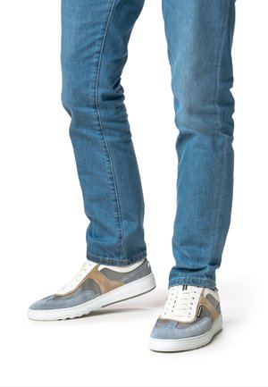 Gray and beige sneakers with mesh panels, white laces, and textured suede. Worn with fitted blue jeans. Minimalistic design.