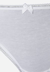Culottes en coton blanc avec une texture douce, dotées d'un nœud décoratif à la taille et d'une délicate bordure en dentelle le long des bords.