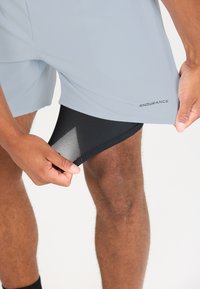 Helle graue Sportshorts mit schwarzem Innenfutter; aus glattem, atmungsaktivem Material; mit ENDURANCE-Logo nahe dem Saum.
