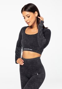 Sort, langærmet crop top og højhalsede leggings i blødt materiale; bemærkelsesværdigt logo på taljen, glat tekstur og tætsiddende design.