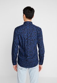 Koszula w panterkę w ciemnoniebieskim i czarnym kolorze, z kołnierzykiem i długimi rękawami. Posiada prosty dół i zapinany na guziki tylny karczek.