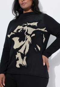 Schwarzer Stricksweater mit einem strukturierten, beigen Blumenmuster auf der Vorderseite, hohem Kragen und langen Ärmeln, mit glatter Stoffoberfläche.