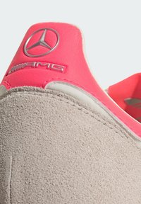 Světlé šedé semišové tenisky s růžovým syntetickým patním tabem, na kterém je stříbrné logo Mercedes-Benz a nápis "AMG" v zvýrazněných písmenech.